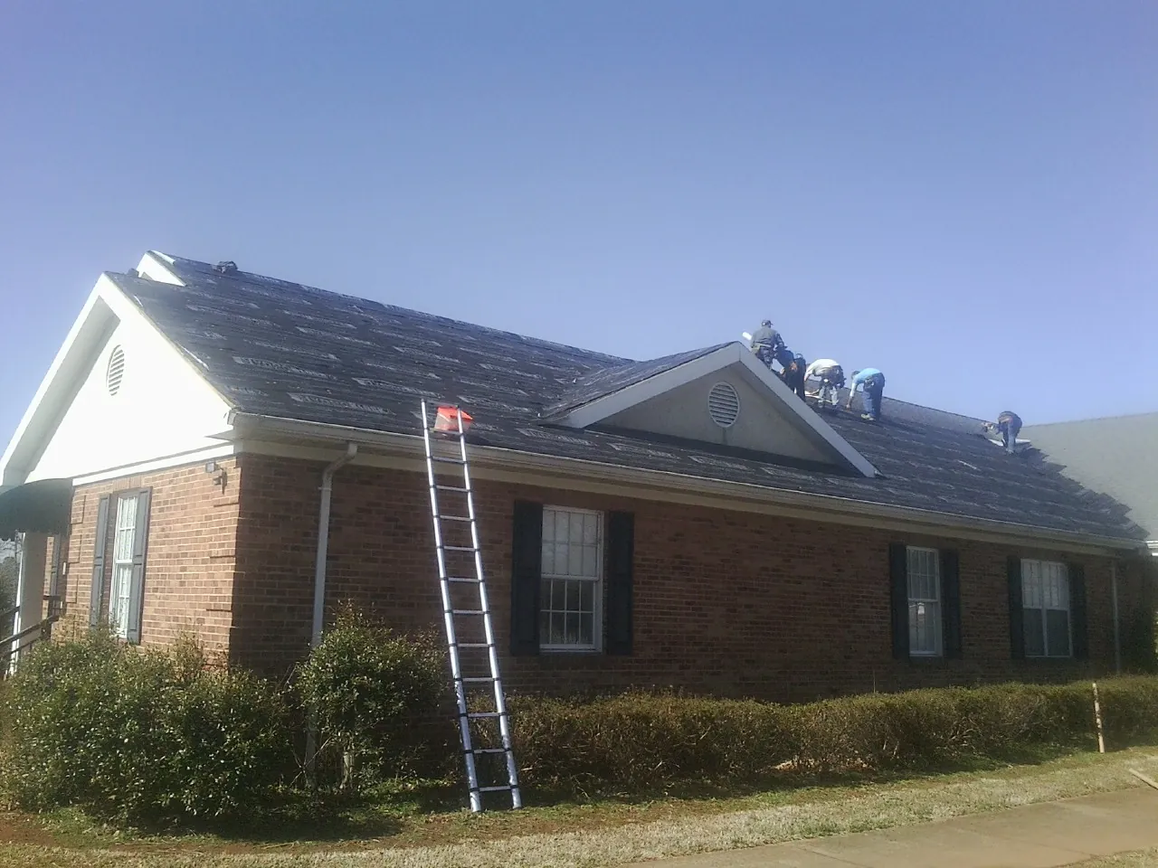 Crew tearing shingles off a brick ranch roof with a ladder set — Metal Roof Repair work by our crew in Thayer