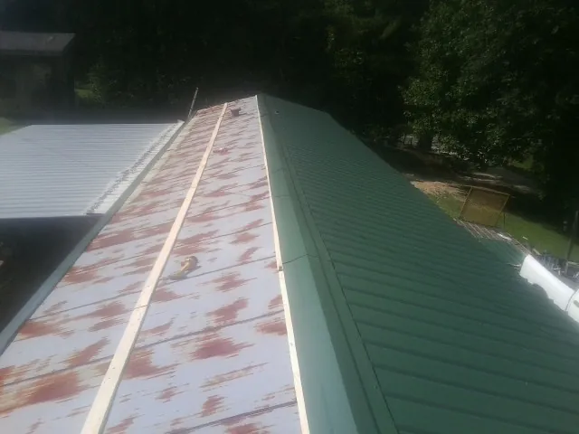Old rusted panels beside newly installed green metal roofing — Wind Damage Roof Repair by Roofing Brothers in Thayer