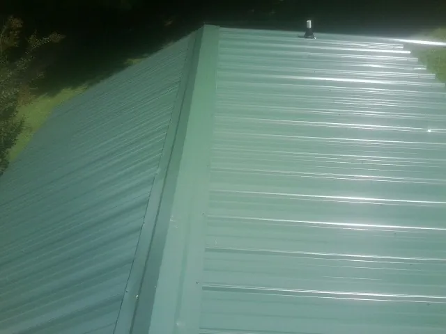 New green metal panels meeting at the ridge of a roof — Flat Roof Repair work by our crew in Thayer