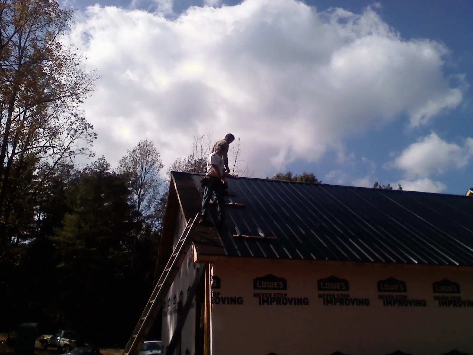 Roofer fastening dark metal panels high against a cloudy sky, from a Roof Inspection job in Thayer